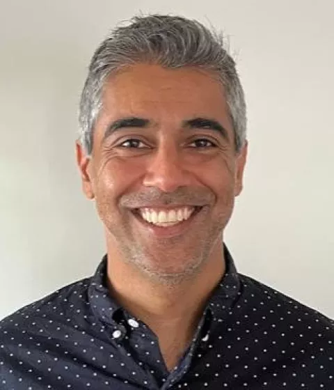 A person in a navy shirt with white dots smiling with a background of bookshelves.