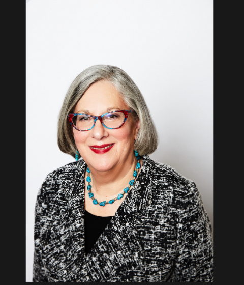 A person in glasses smiling against a white background.