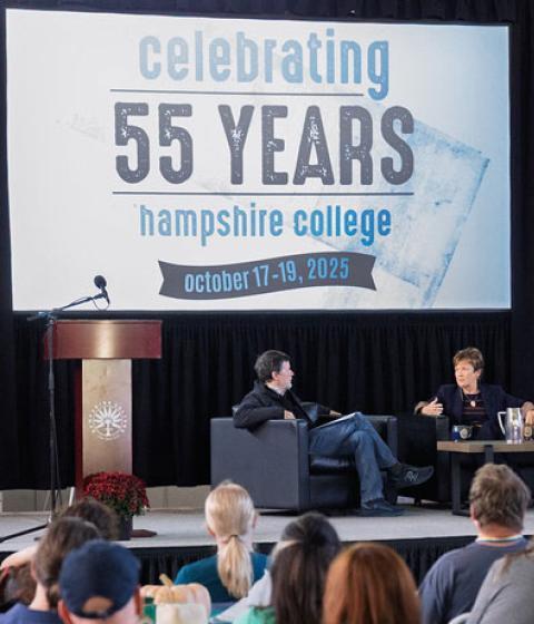 Ken Burns, Lynn Pasquerella, and Gary Marcus sit on a stage under a banner reading Celebrating 55 Years
