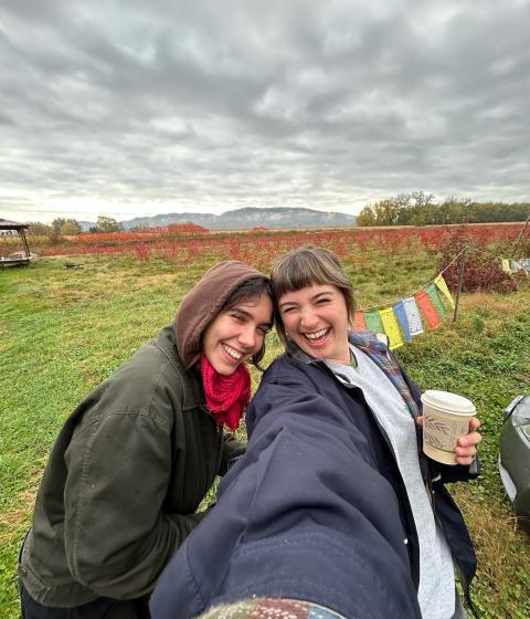 Two people taking a selfie and smiling with a green landscape in the background.