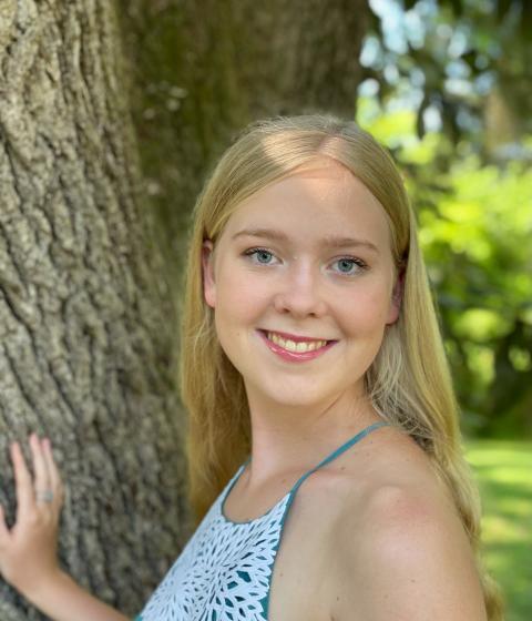 A person in a tank top stands by a tree smiling.