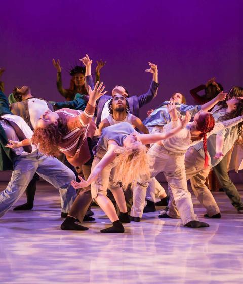 Dancers in a group leaning back with purple lighting