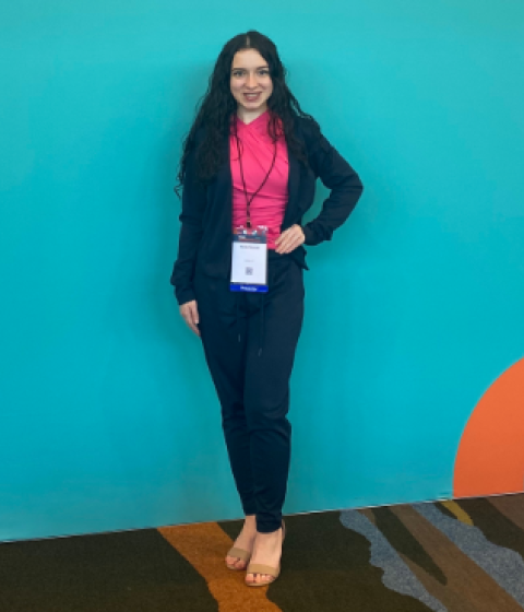 A person in a pink shirt and blue suit posing in front of a bright blue wall.