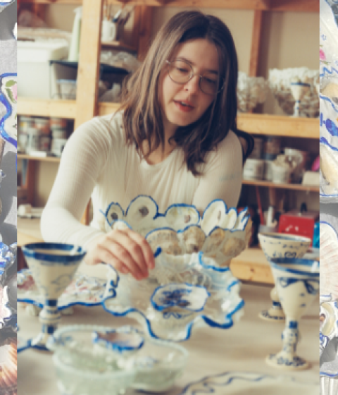 A person in classes and a white shirt painting a ceramic item with a background of colorful ceramic dishes.