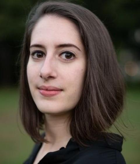 A close up of a person with a brown bob and a black shirt standing outside.