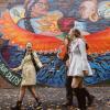 Three students walk past a mural. 